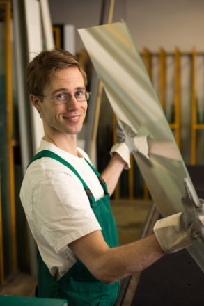 Worker in glazier's workshop or glass warehouse handling glass